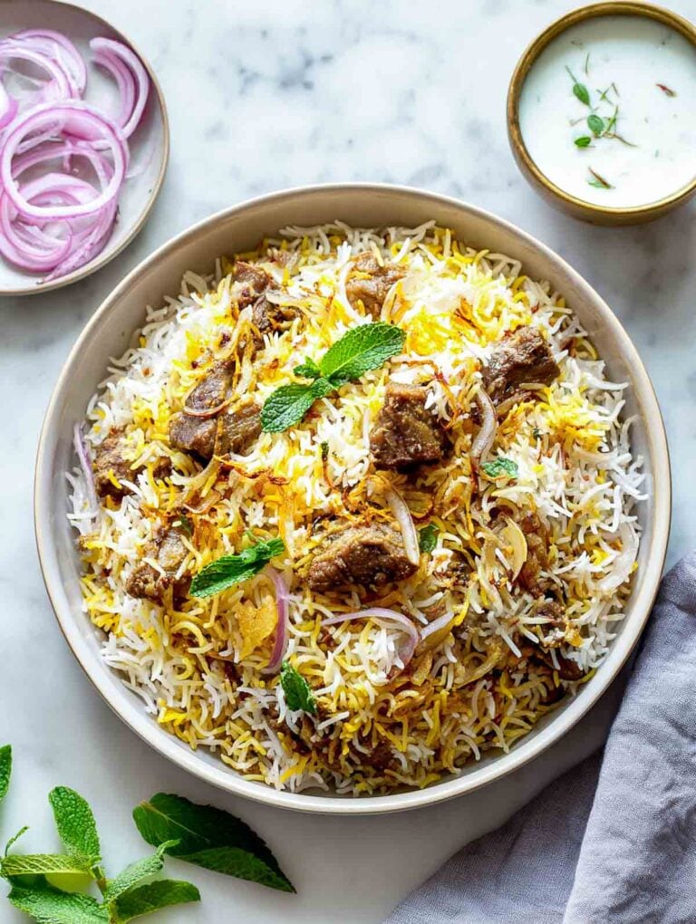 A bowl of lamb biryani topped with fried onions and mint leaves.