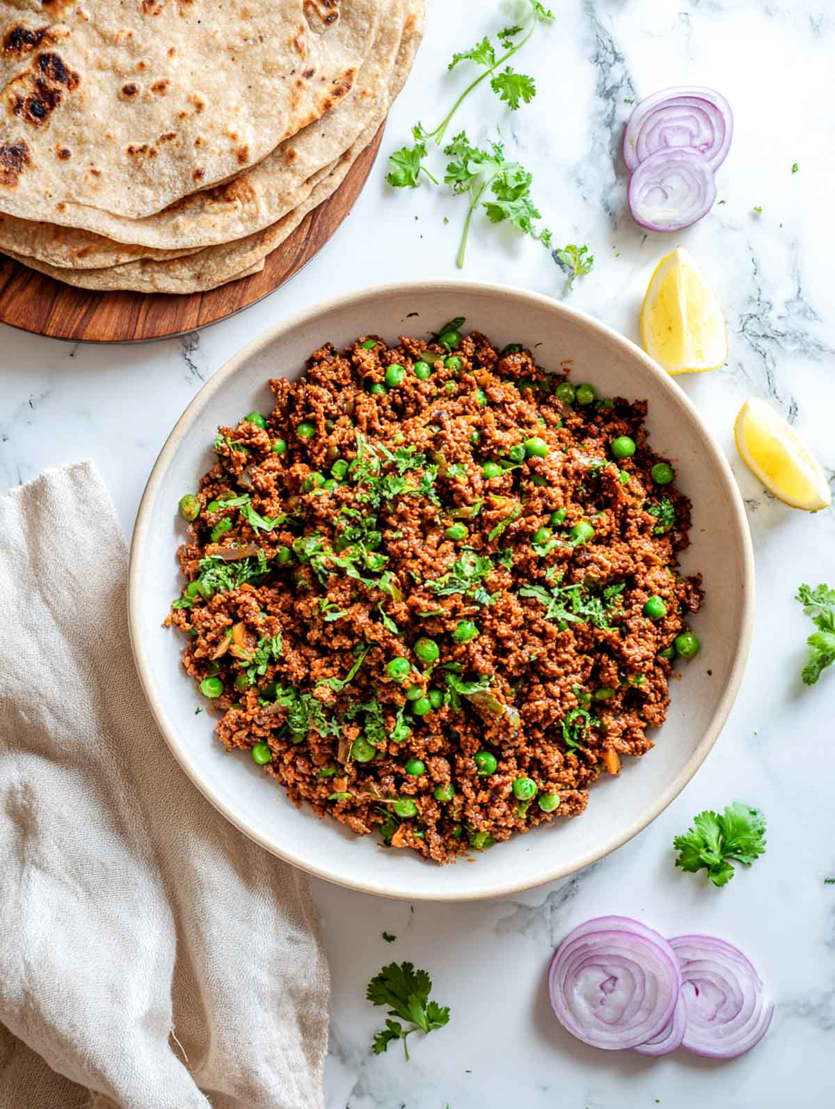 Dry lamb keema with peas is served in a bowl alongside stacked rotis.