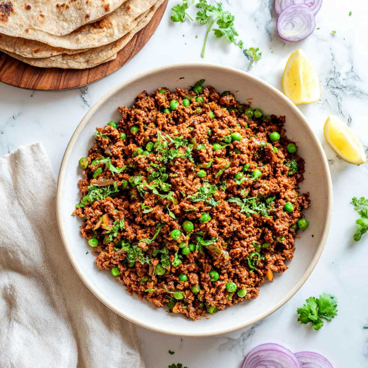 Dry lamb keema is served family-style with rotis, lemon wedges, and cilantro.