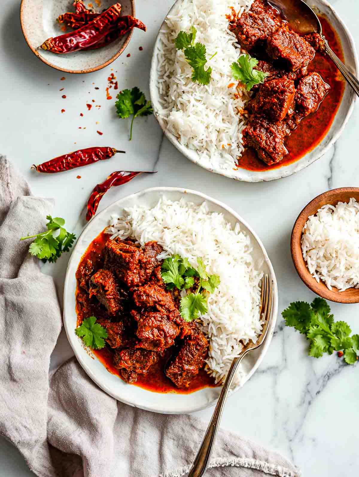Plated lamb vindaloo served with basmati rice on white ceramic plates.