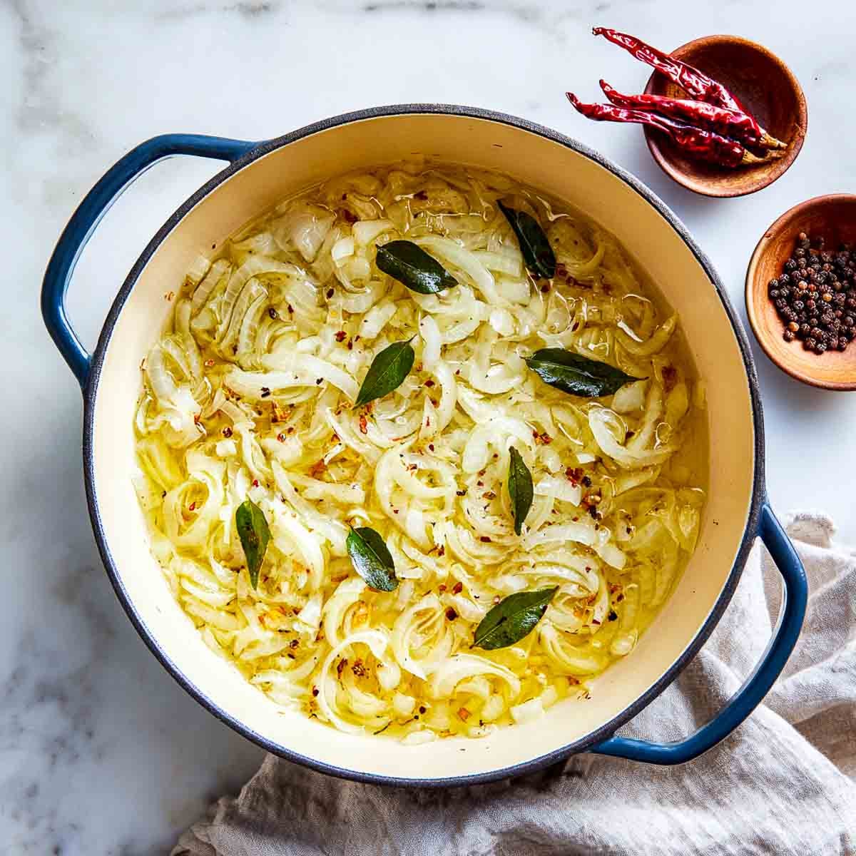 Sliced onions frying with curry leaves in a cast iron Dutch oven.