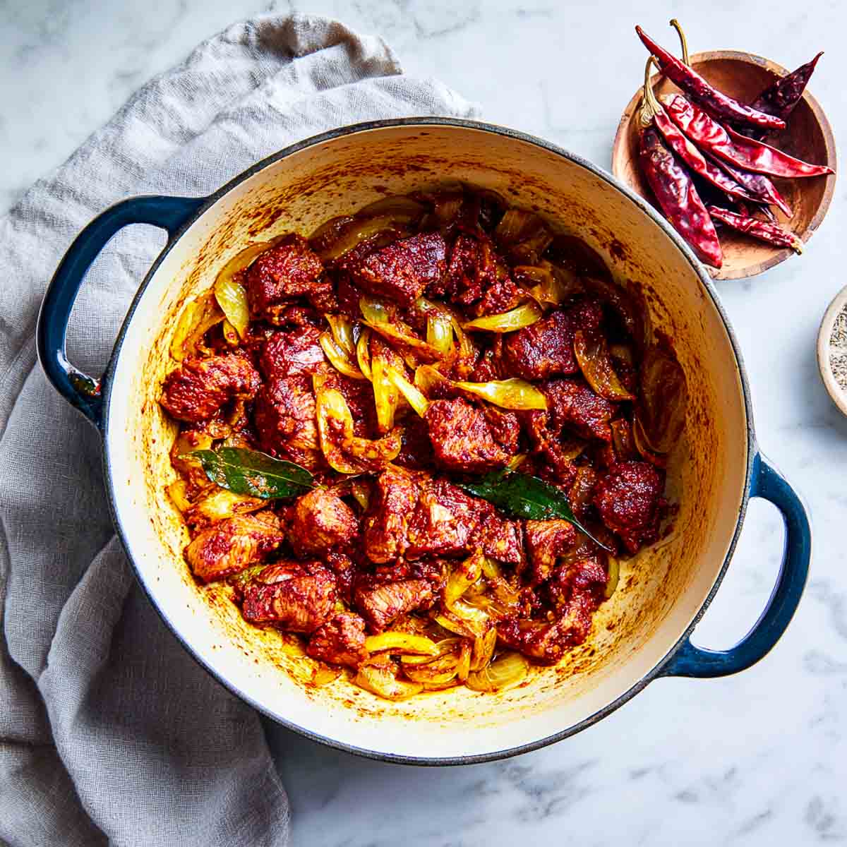Marinated lamb added to onions and curry leaves in a Dutch oven.