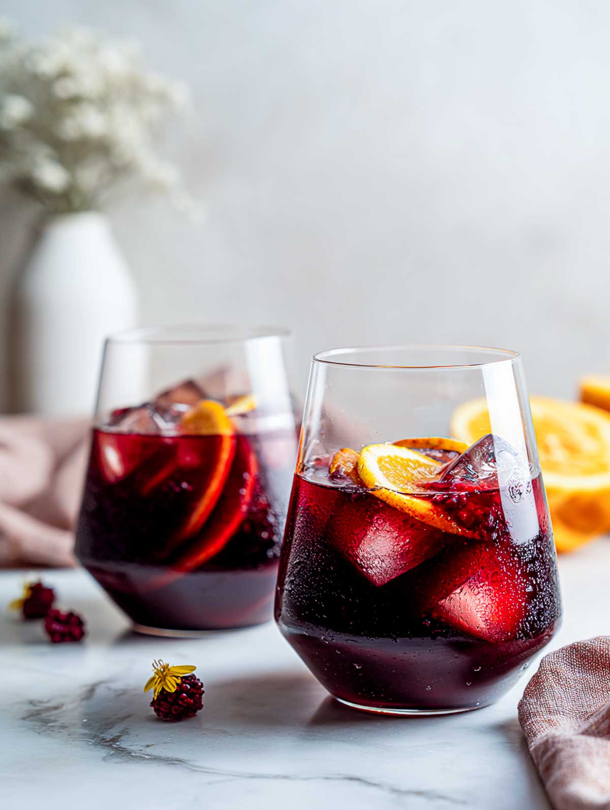 Side view of two red wine love sangrias in stemless glasses on a white marble surface.
