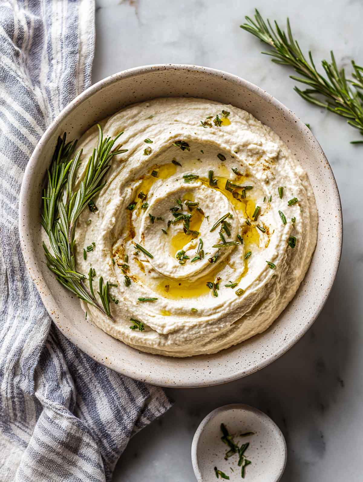 Rosemary white bean dip with olive oil swirl in ceramic bowl.