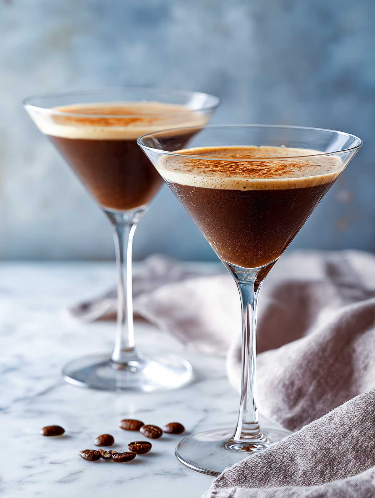 Side view of two vanilla rose espresso martinis in martini glasses on a white marble surface.