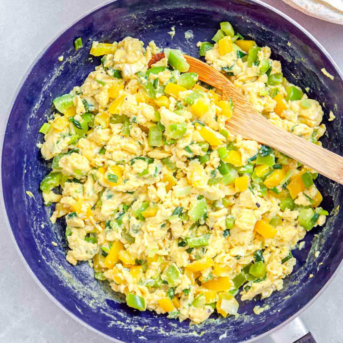 Scrambled eggs with bell peppers and scallions cooking in a skillet.