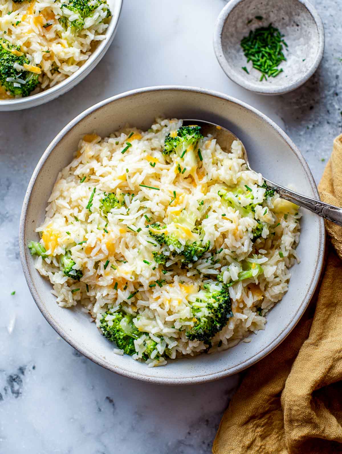 Broccoli cheddar style rice cooker rice with melted cheese and chives in a bowl.