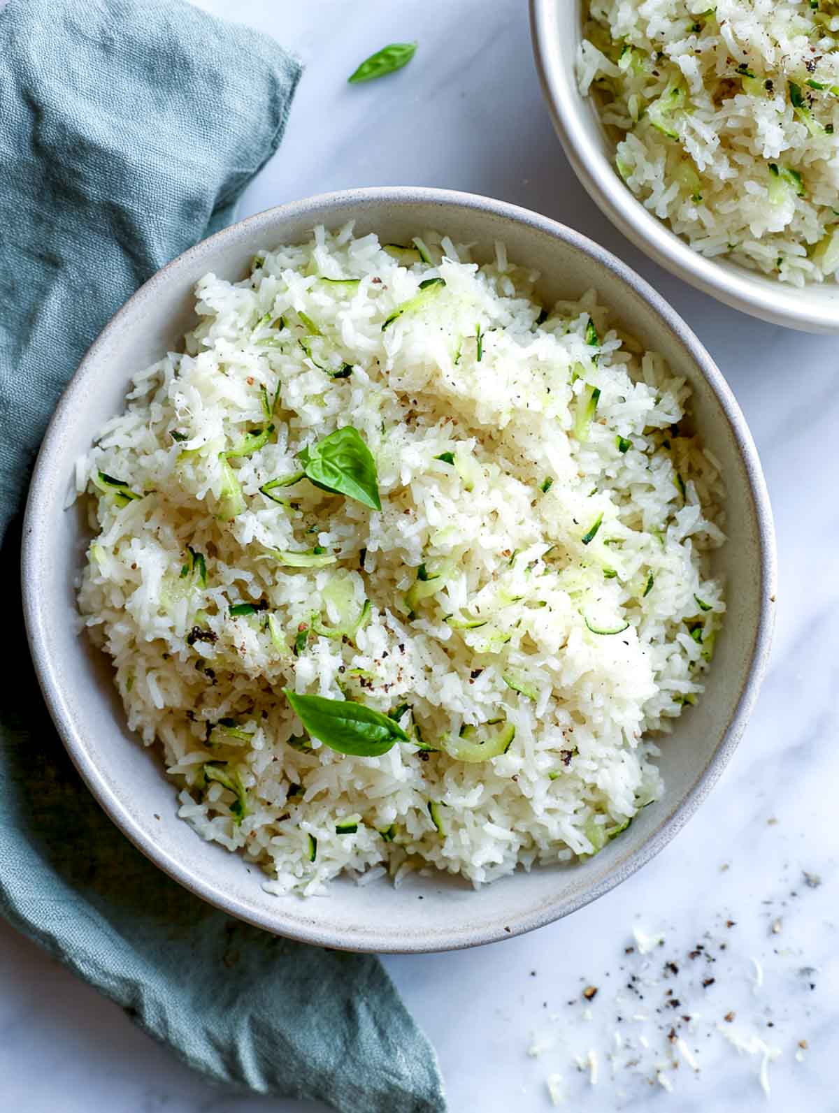 Buttery zucchini rice in a bowl with basil on a white marble surface.