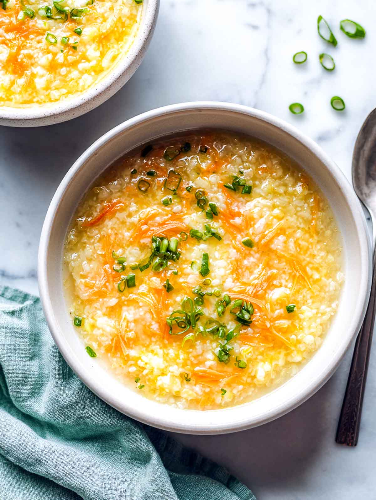 Carrot ginger rice cooker congee topped with scallions in a ceramic bowl.