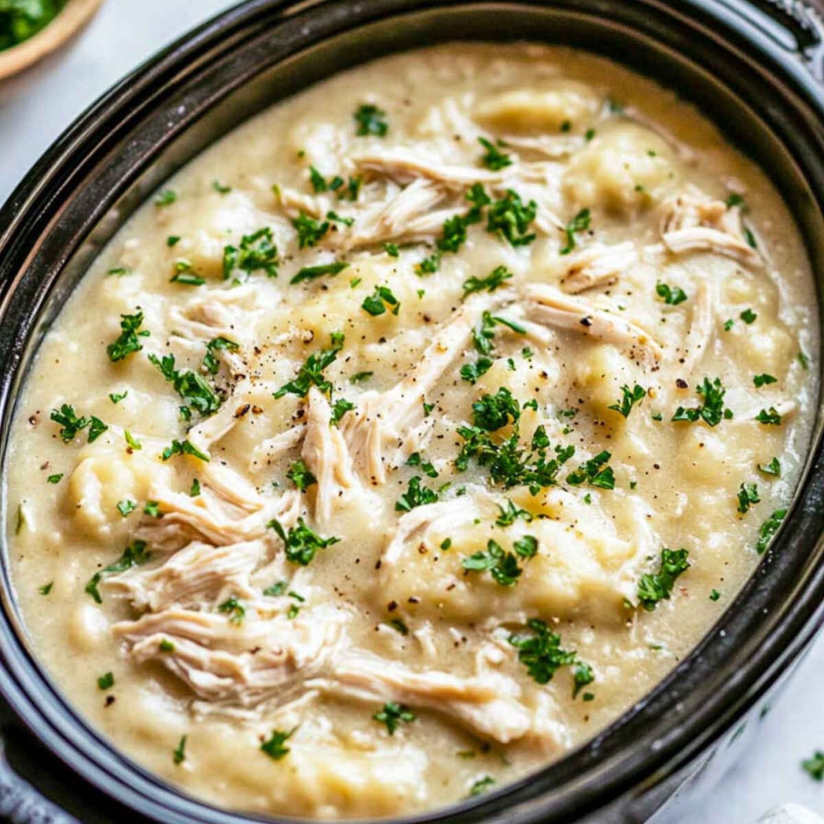 Chicken and dumpings in a crockpot placed on a white marble surface.