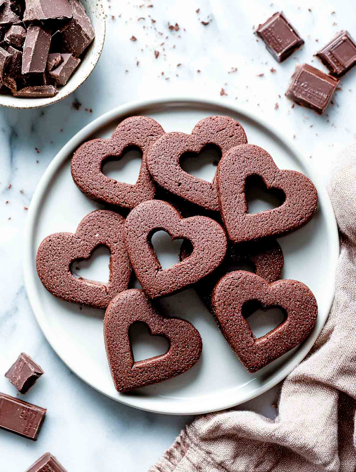 Chocolate sugar cookies with heart cutout centers on a white plate.