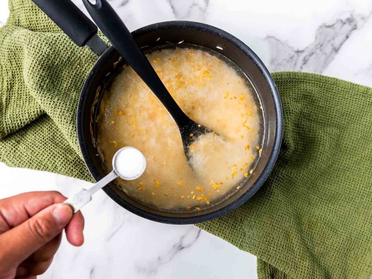 Water being poured into a saucepan with rice and vermicelli, beginning the simmering step of garlic rice.