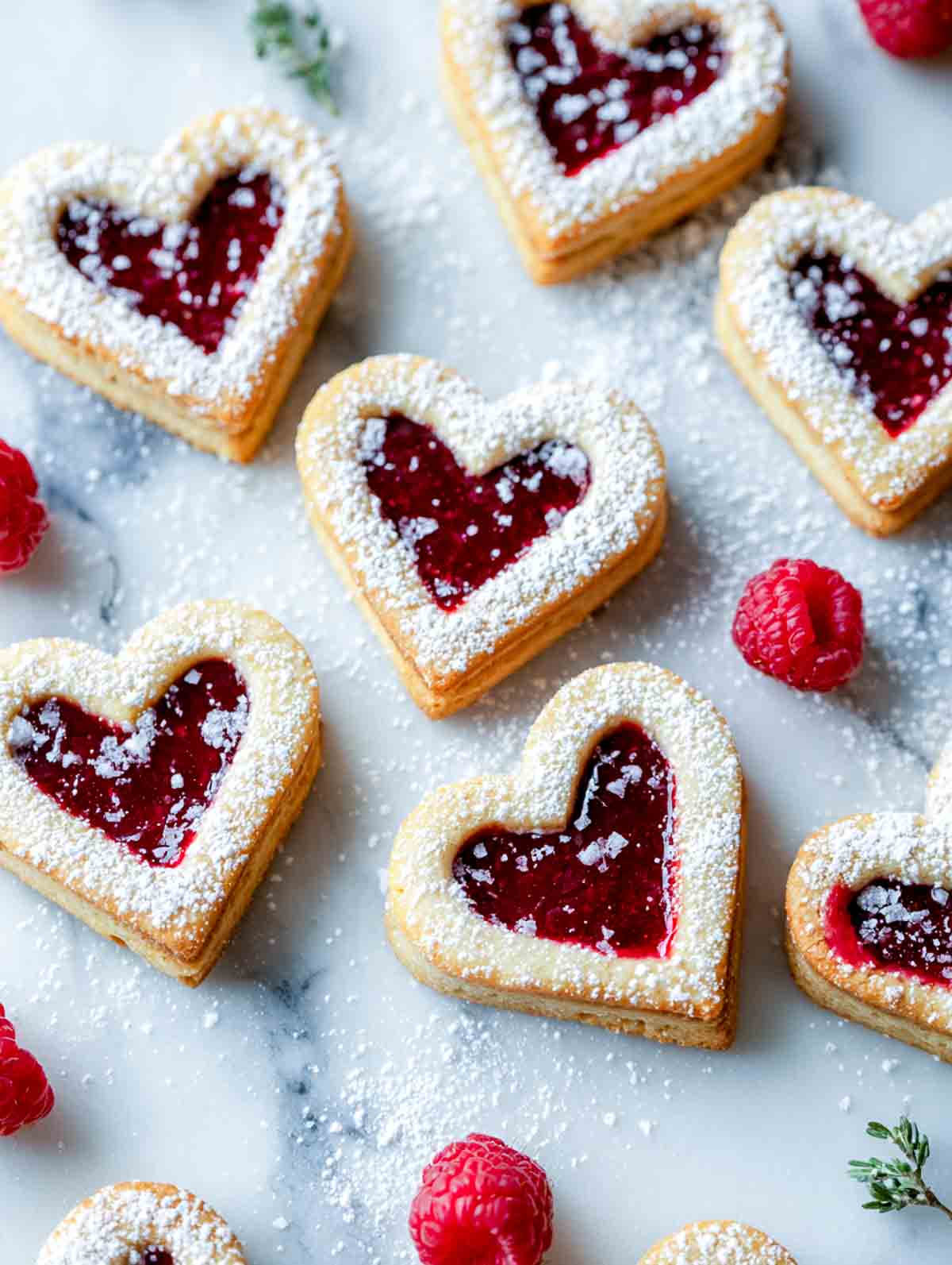 Heart shaped linzer cookies with raspberry filling on a white marble surface.