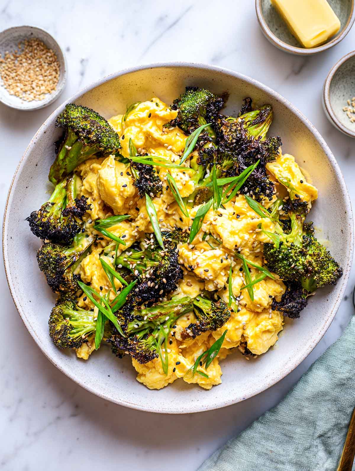 Top-down view of a shallow ceramic bowl filled with soft, fluffy scrambled eggs coated in miso butter and mixed with deeply roasted broccoli florets.
