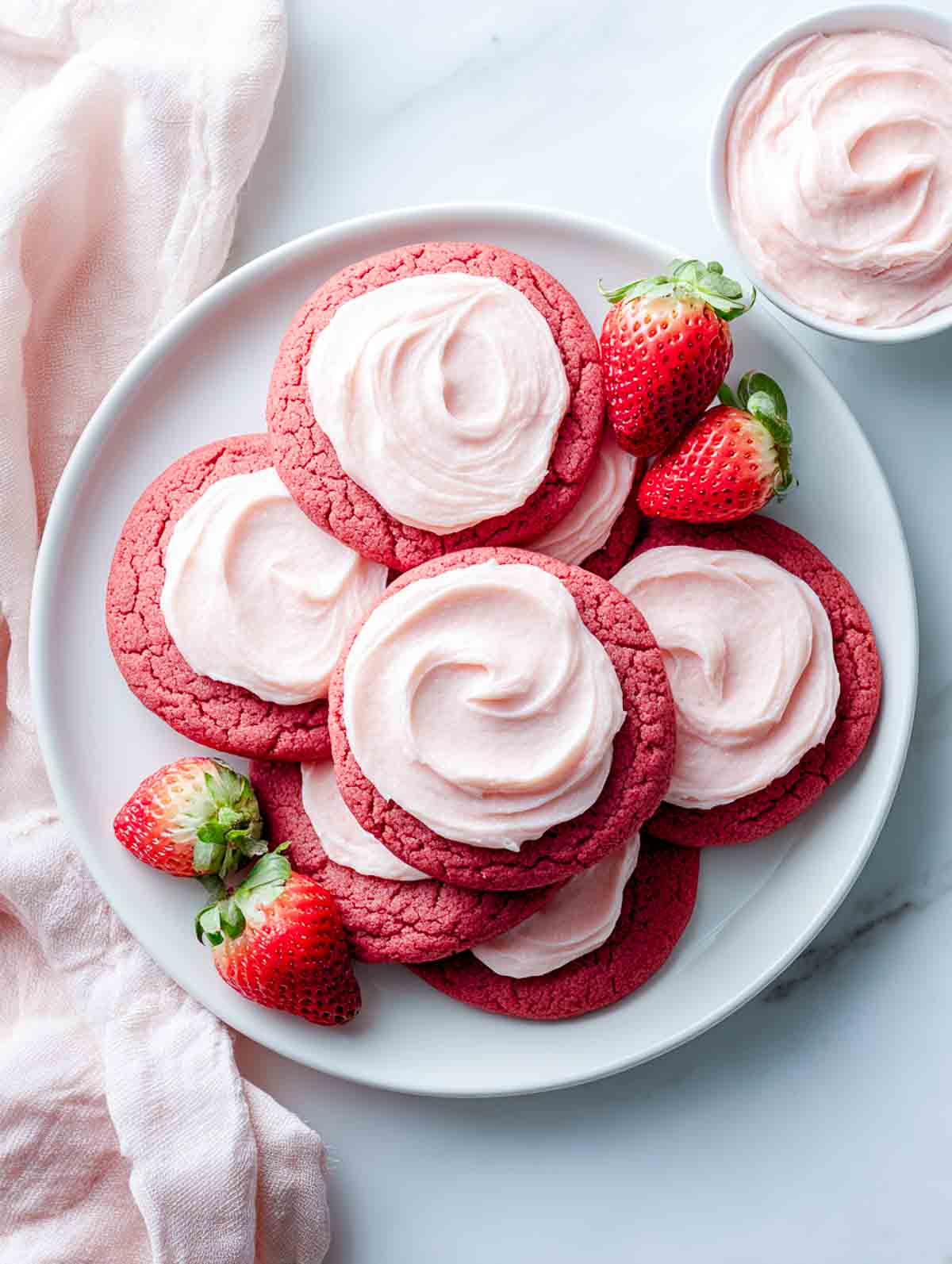 Red sugar cookies with strawberry frosting swirls on a white plate.