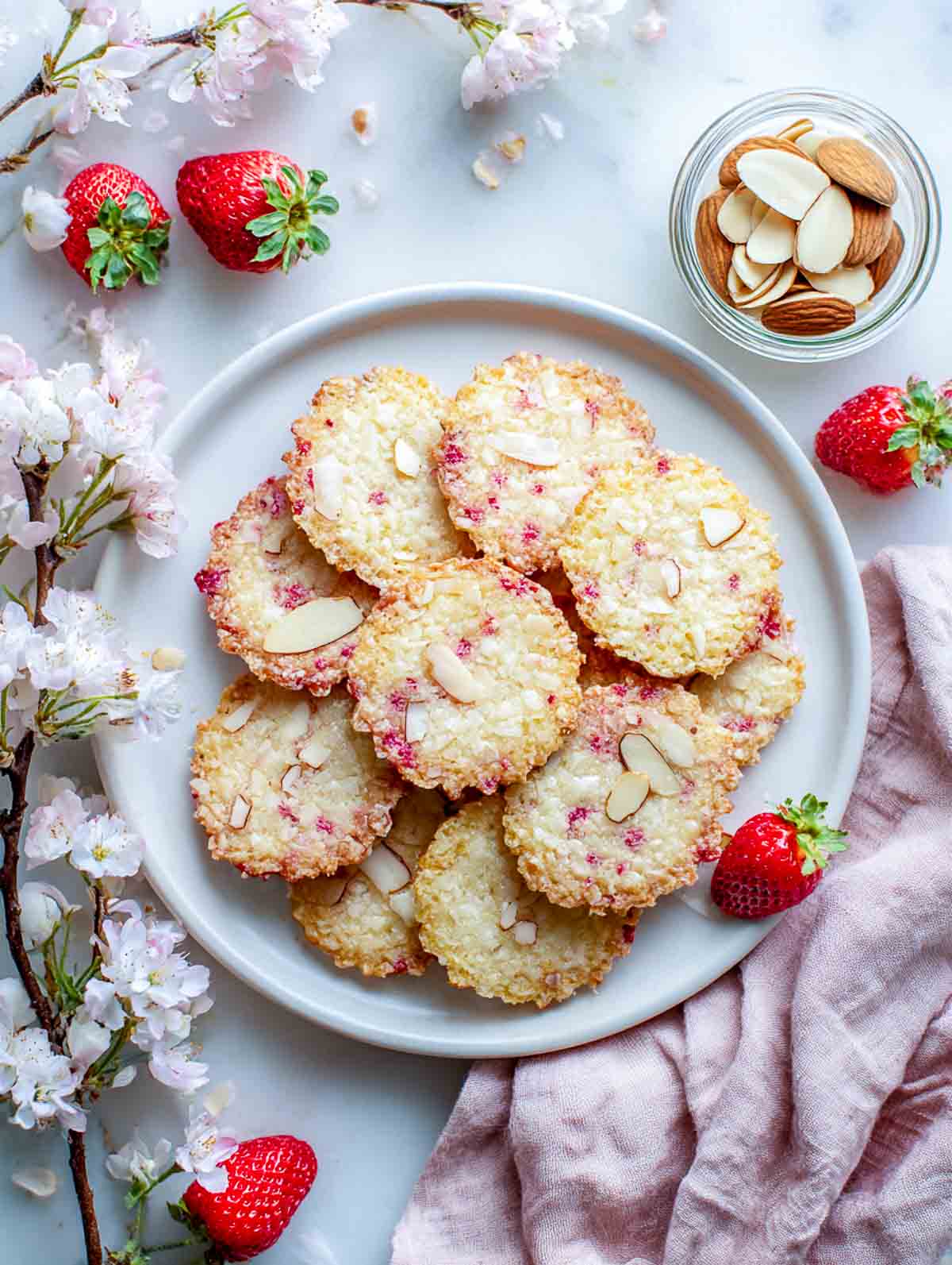 Thin strawberry almond lace cookies with sliced almonds on white plate.