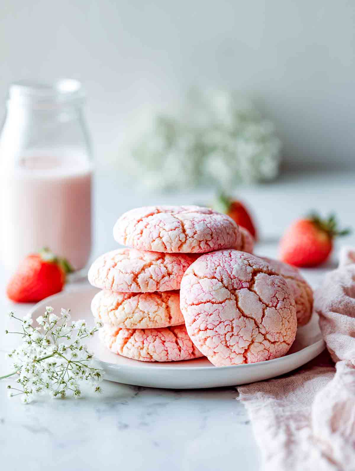 Strawberry milk cookies with pink crackle tops stacked on a plate.