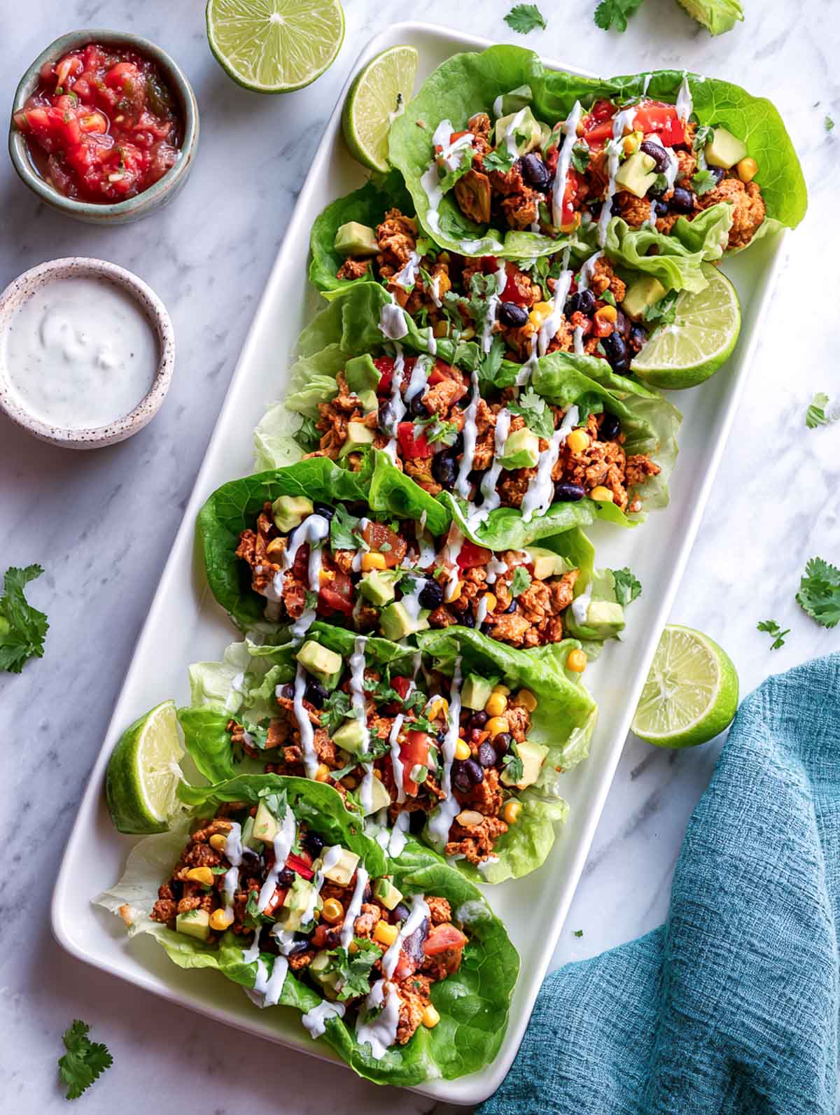 Tex-mex chicken lettuce cups on a white rectangular serving plate with salsa in the background.