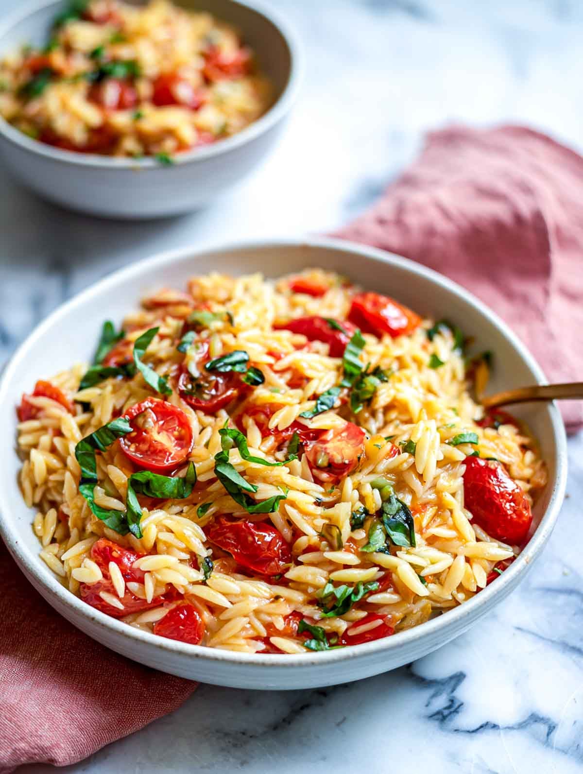 Tomato basil rice cooker orzo with cherry tomatoes and fresh herbs in a white bowl.