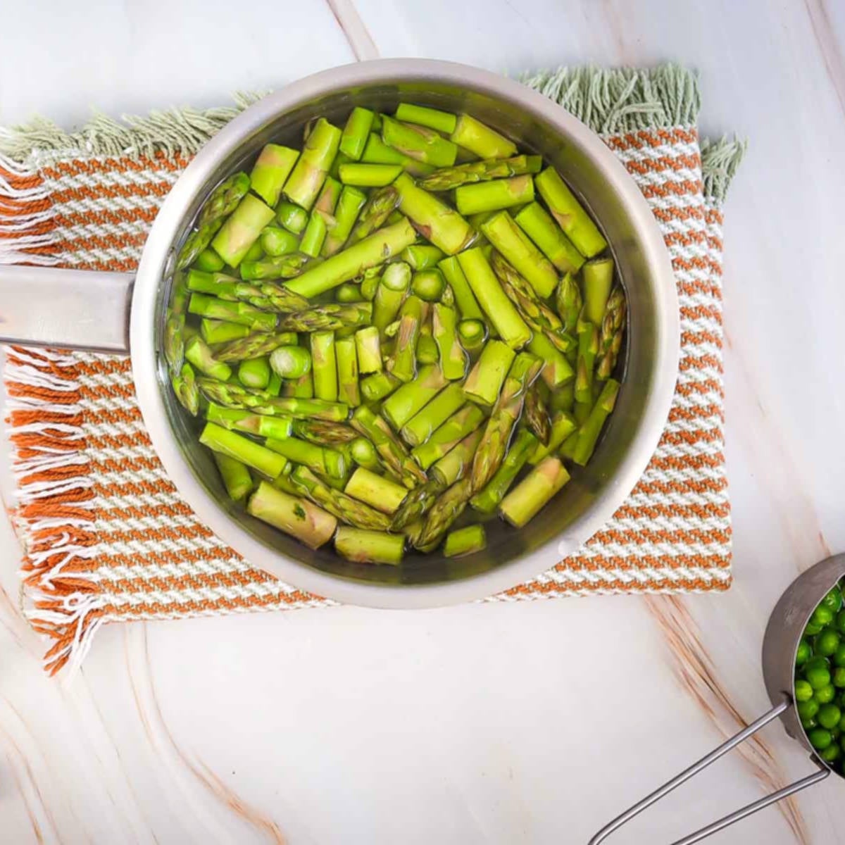 Asparagus and peas soaking in a pot of water on a striped kitchen towel.