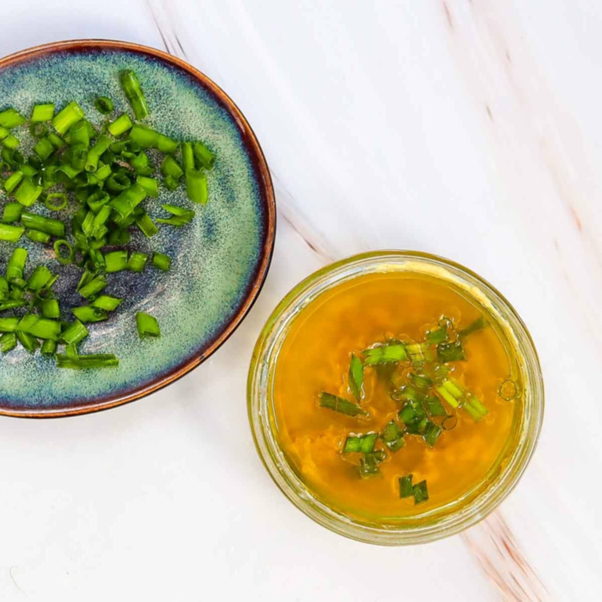 Small bowl of lemon dressing topped with chopped green onions beside a plate of sliced green onions.