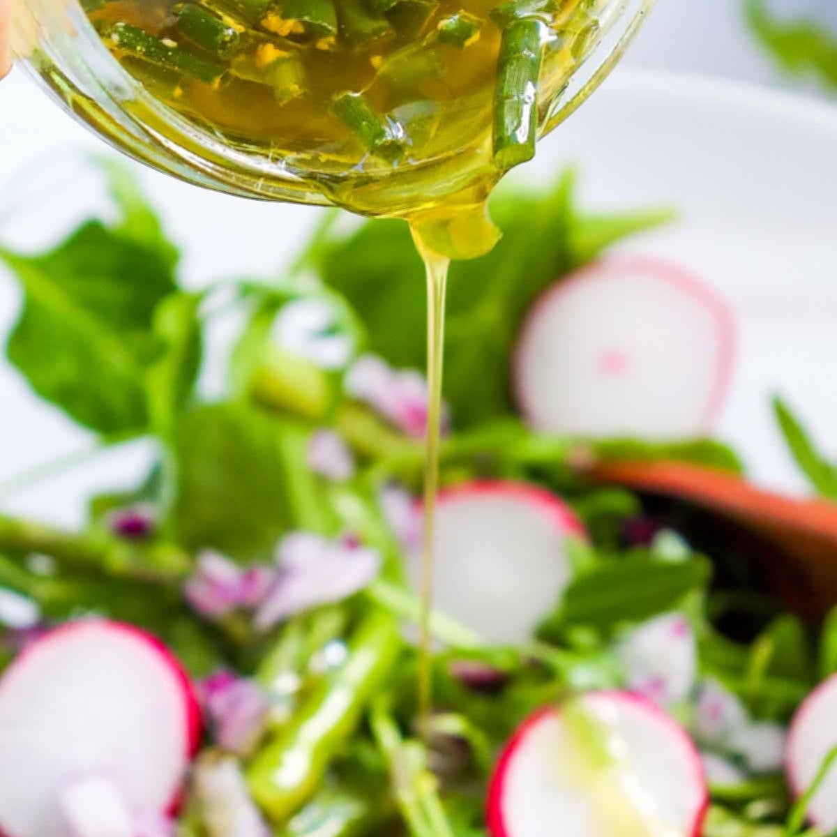 Lemon dressing being poured over a fresh asparagus and radish salad.