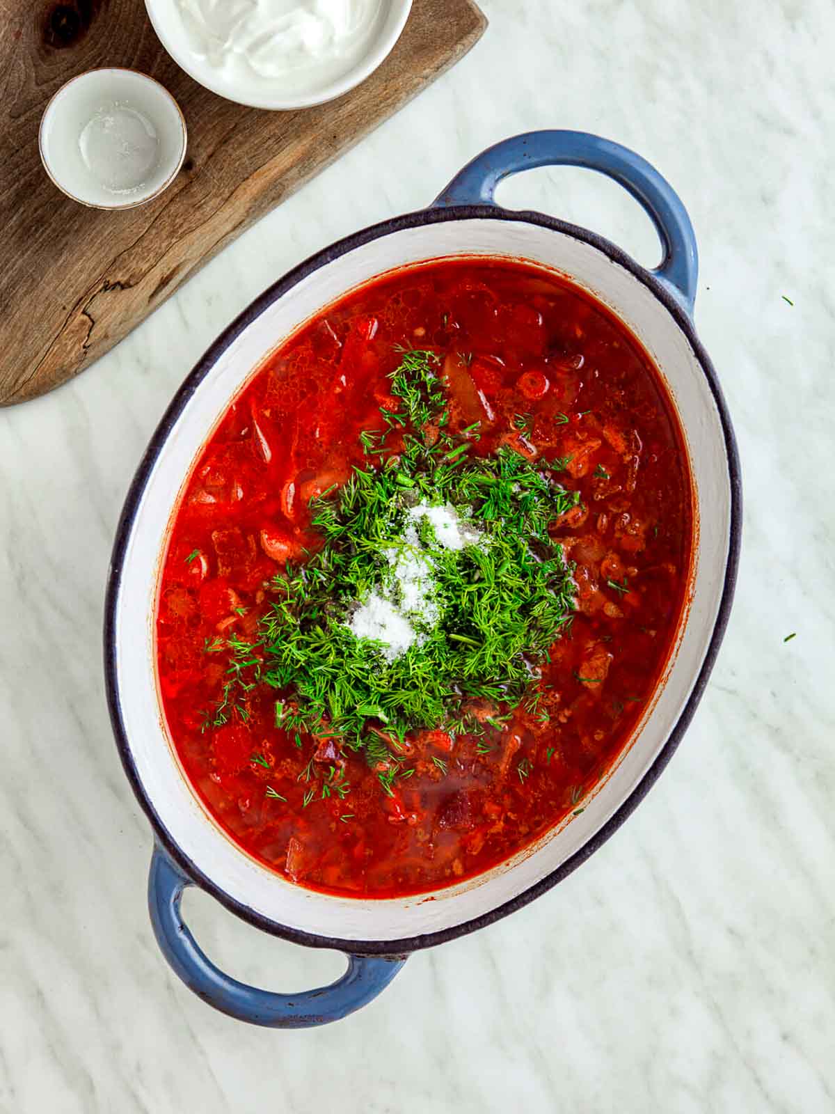 Finished beet borscht in a blue pot, topped with fresh dill and a dollop of sour cream.