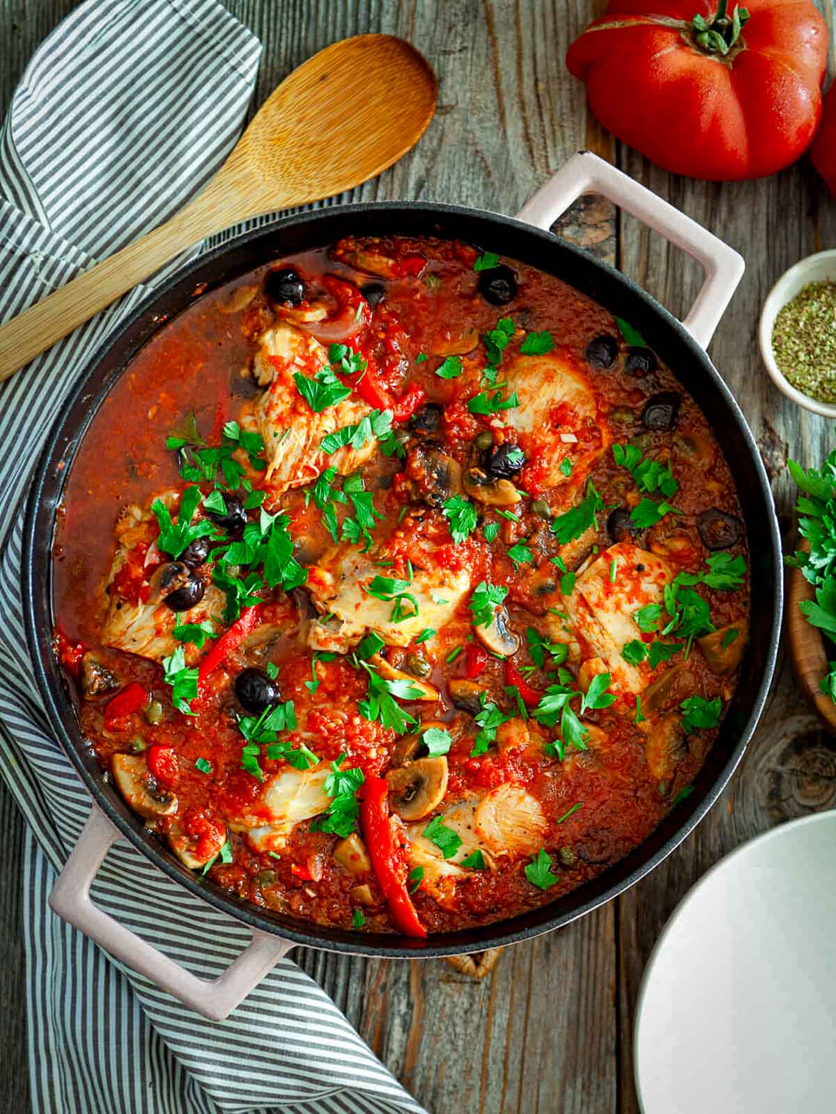 A skillet of classic chicken cacciatore simmered in a rich tomato sauce with mushrooms, olives, and red peppers, garnished with fresh parsley and served on a rustic wooden table.