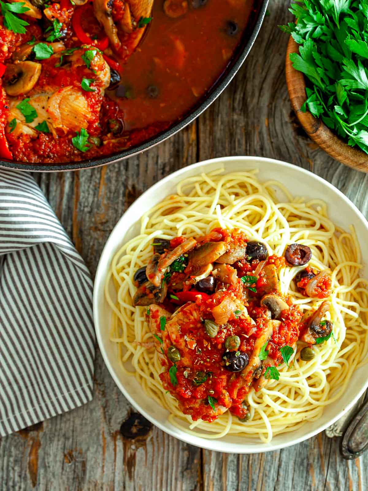 Top-down view of spaghetti served with chicken cacciatore, featuring tender chicken, capers, mushrooms, and fresh herbs.