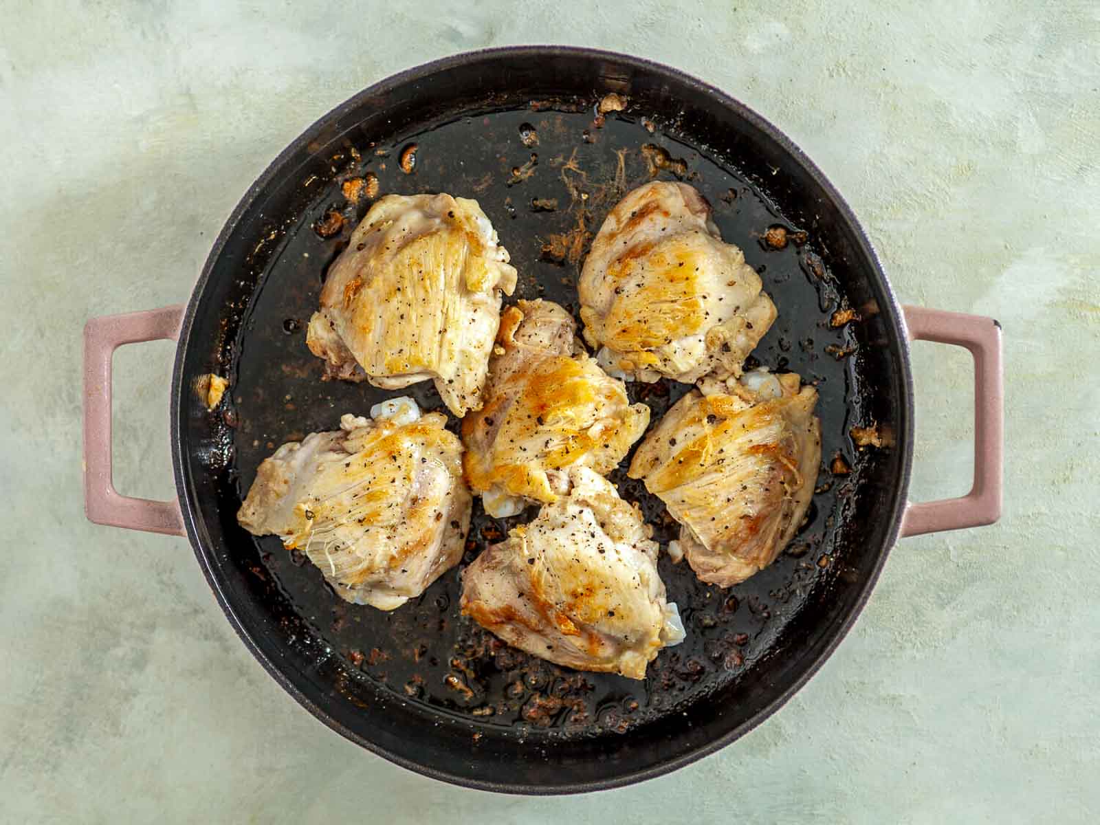 Chicken thighs searing in a skillet until golden brown.