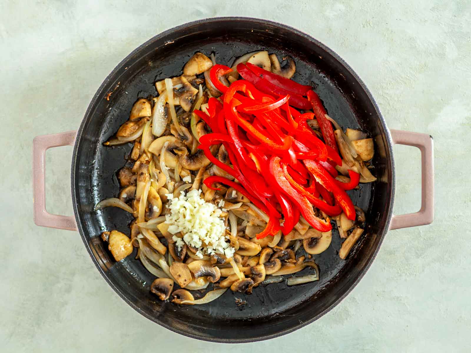 Sautéed mushrooms and onions with sliced red peppers and minced garlic in a skillet.
