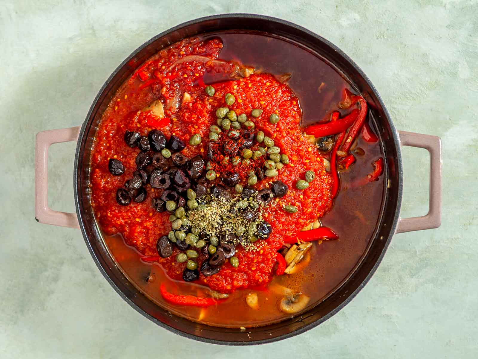 Tomato sauce, olives, capers, and peppers added to the skillet.