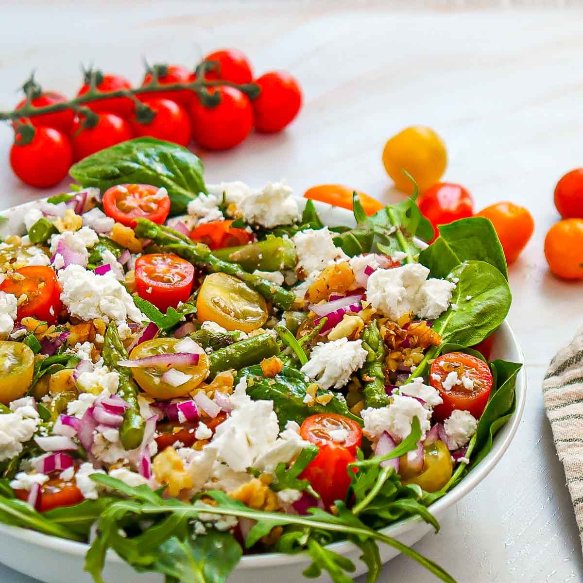 Close-up of goat cheese and asparagus salad with arugula, cherry tomatoes, red onion, and chopped walnuts, served in a white bowl