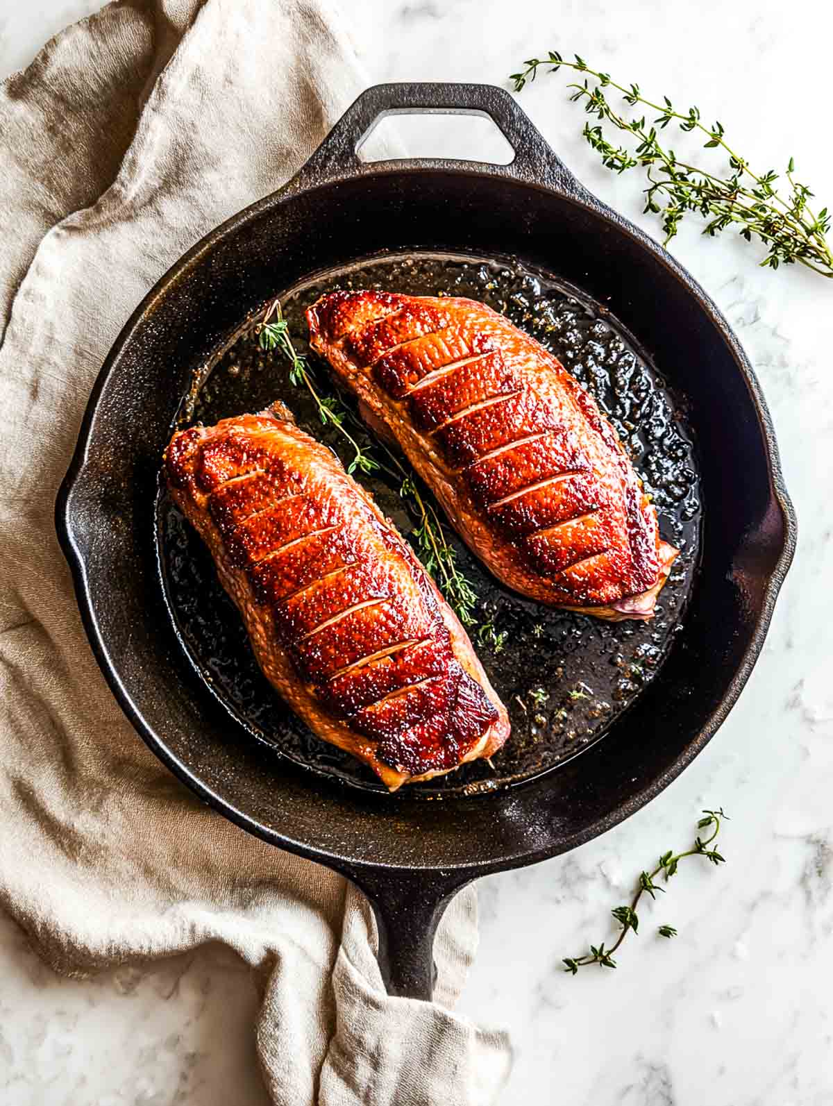 Two duck breasts with crispy skin cooking in a cast iron skillet.