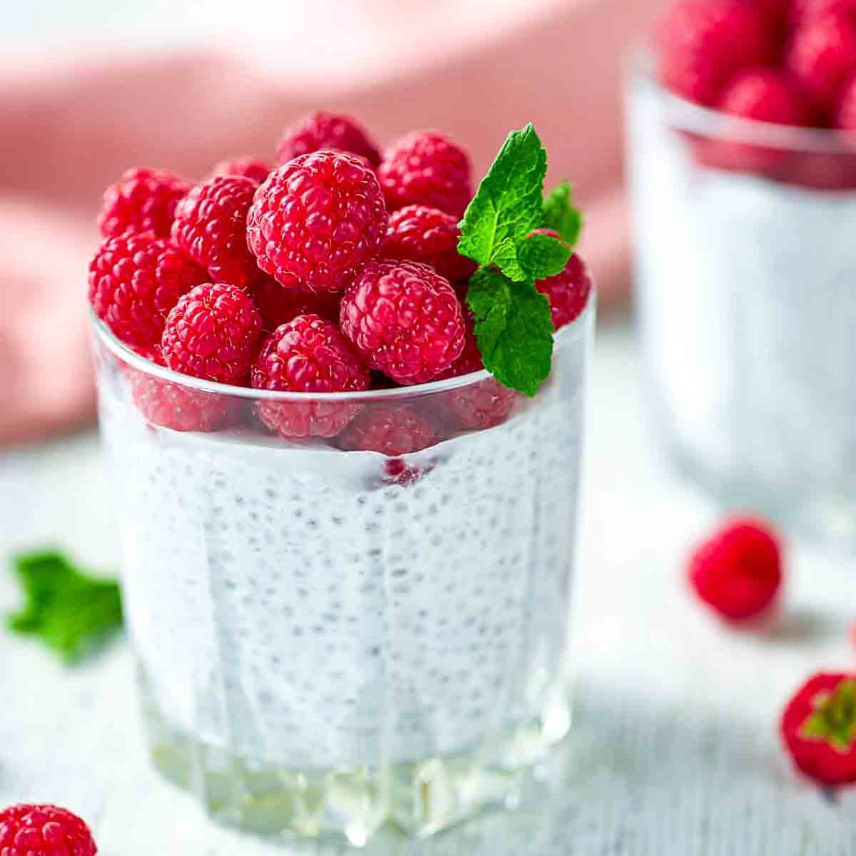 Creamy chia pudding in a glass topped with fresh raspberries and a mint leaf
