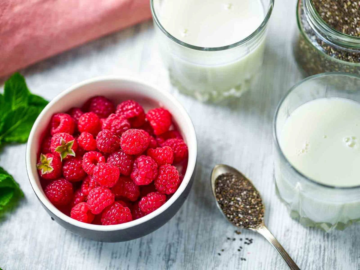 Fresh raspberries in a bowl with chia seeds and milk ingredients for chia pudding