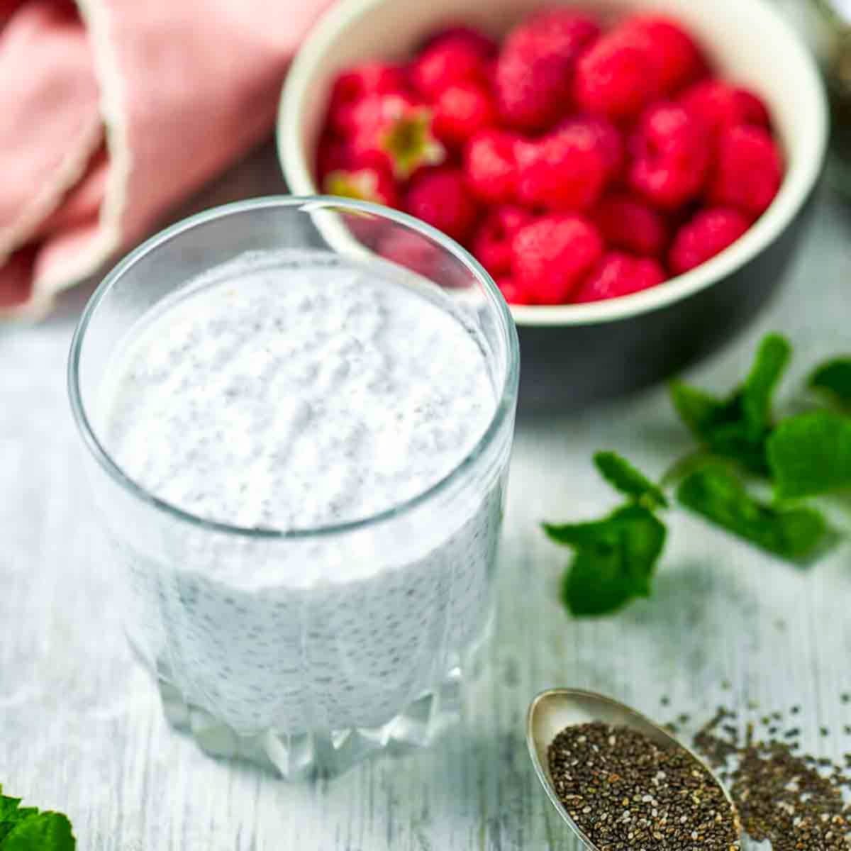 Glass of set chia pudding topped with fresh raspberries and mint on a light surface