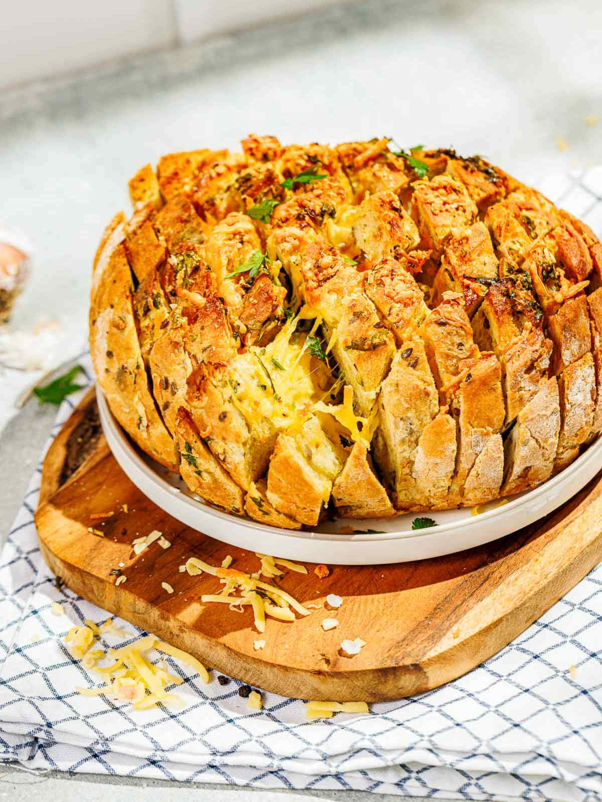 A boule of cheesy garlic pull-apart bread on a wooden board ready to be served.