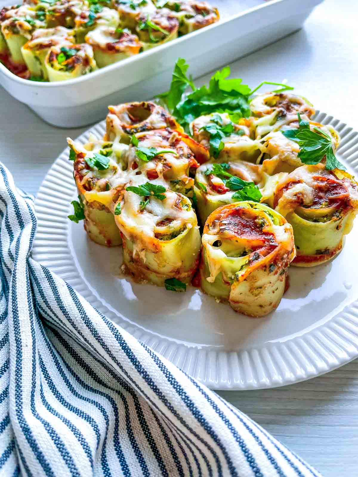 Side view of lasagna roll ups served on a white place with the baking dish in the background.