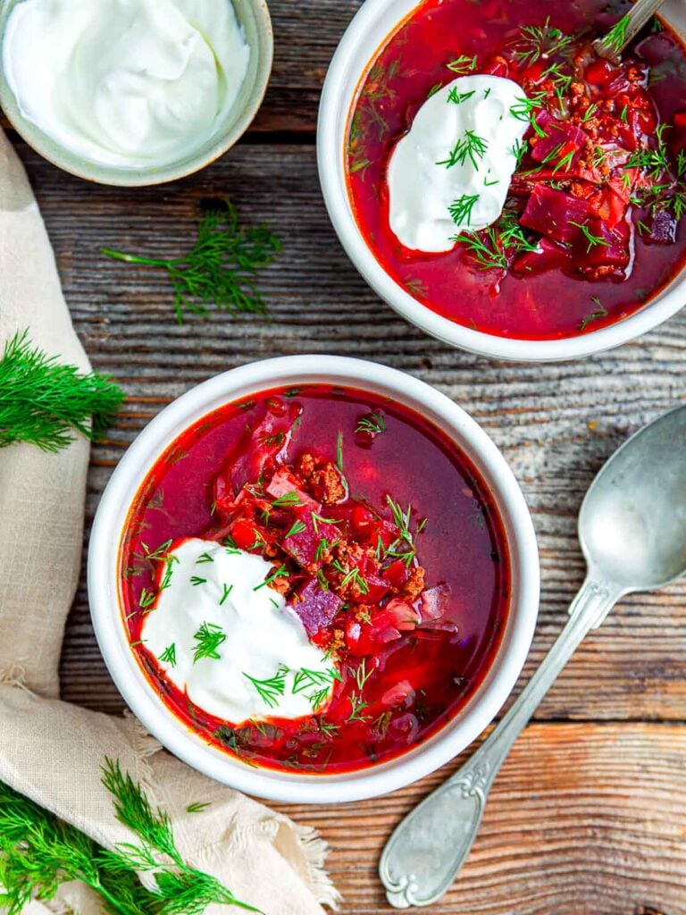 Two bowls of vibrant beet borscht served with generous dollops of sour cream and sprinkled with fresh dill.