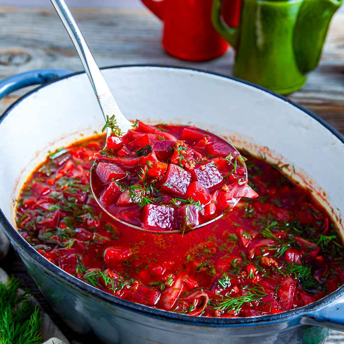 A pot of vibrant beet borscht soup scooped on a ladle and garnished with fresh dill.