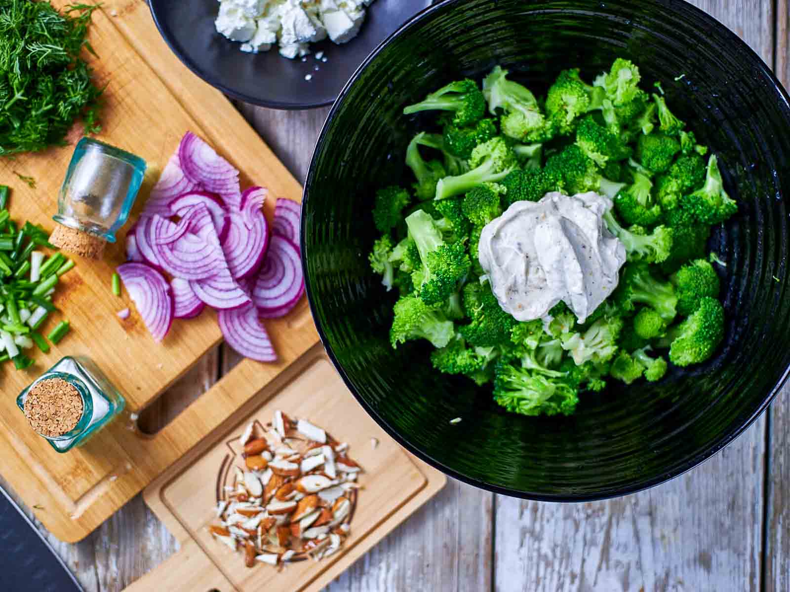 Creamy dressing added to broccoli florets in a large mixing bowl.