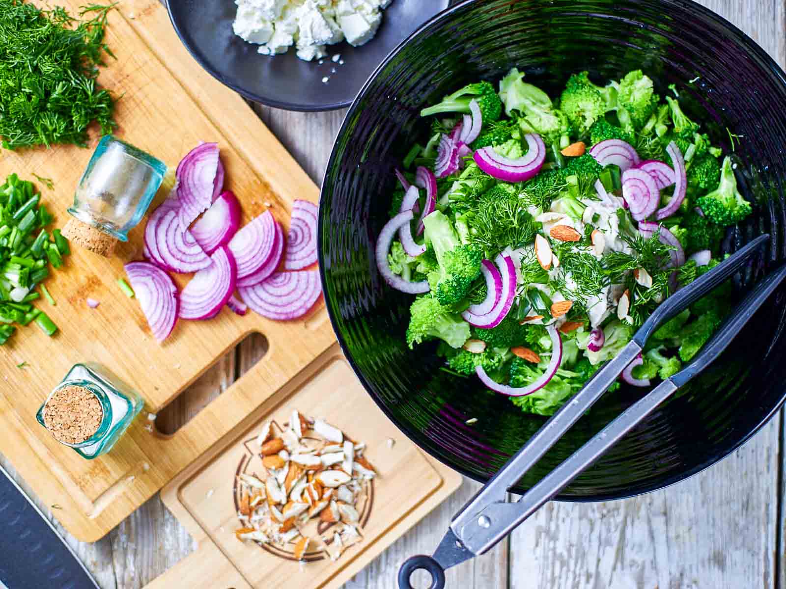 Broccoli salad with feta, red onion, dill, and almonds in a mixing bowl.