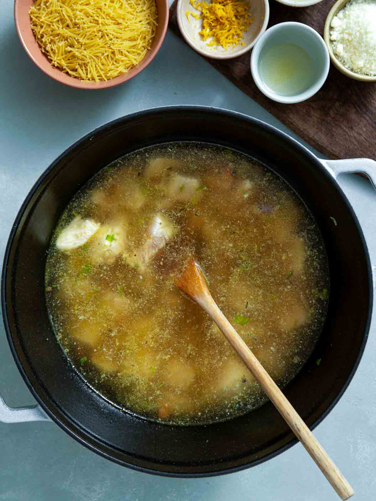 Chicken and vegetables simmering in broth in a pot with a wooden spoon.
