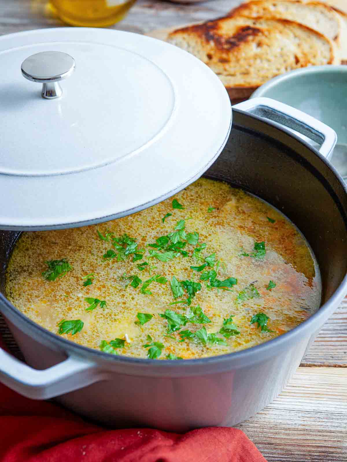 Pot of chicken fideo soup garnished with parsley and partially covered with a lid.