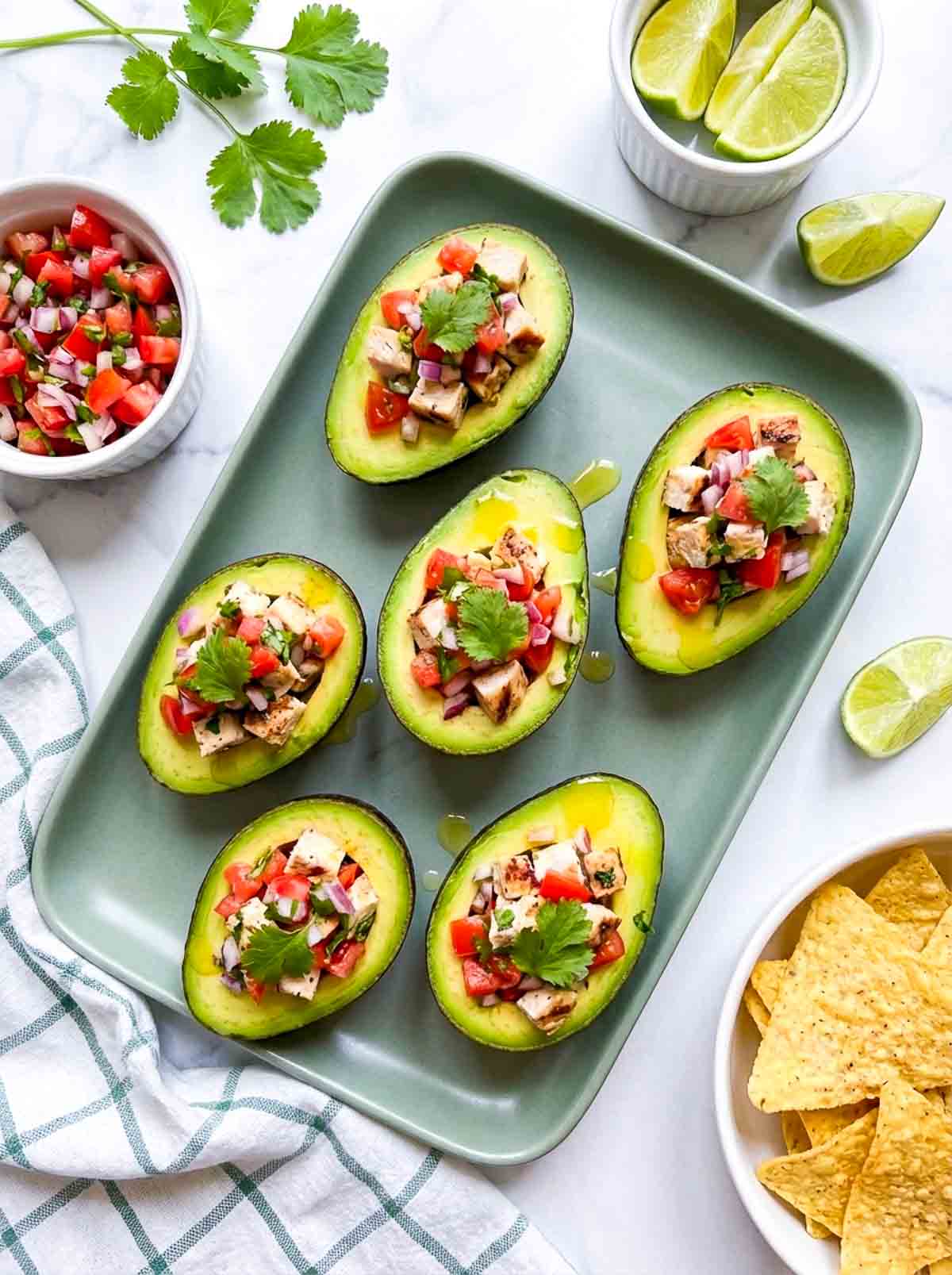 Avocados stuffed with pico de gallo and chicken and served on a green tray.