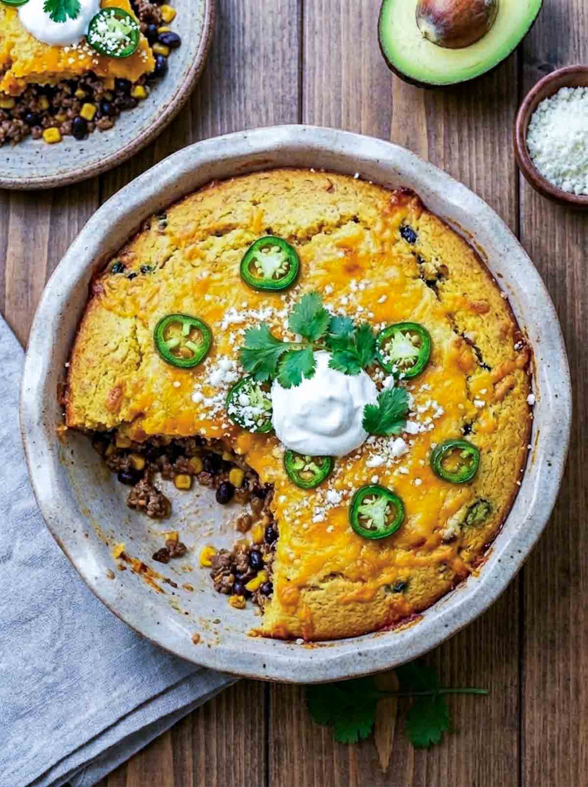 Top view of cornbread taco casserole bake with a sliced scooped out and served on a plate.