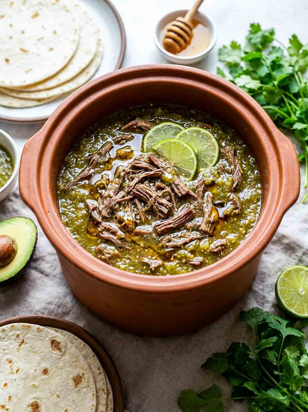 Salsa verde shredded beef in a rustic bowl with tortillas in the background.