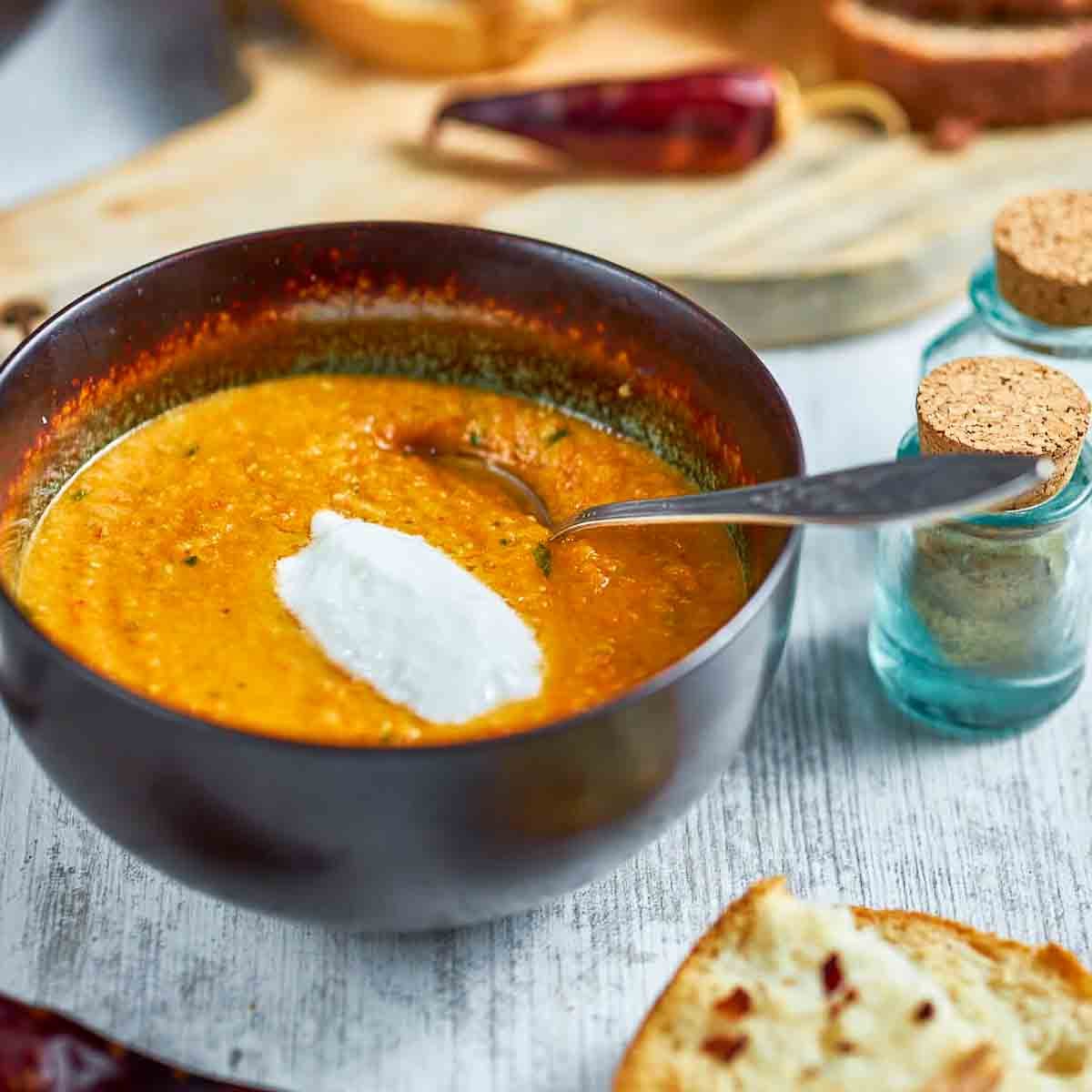 A close-up shows a person’s lower face alongside a bowl of creamy carrot lentil soup, highlighting both the dish and a clean, minimal aesthetic