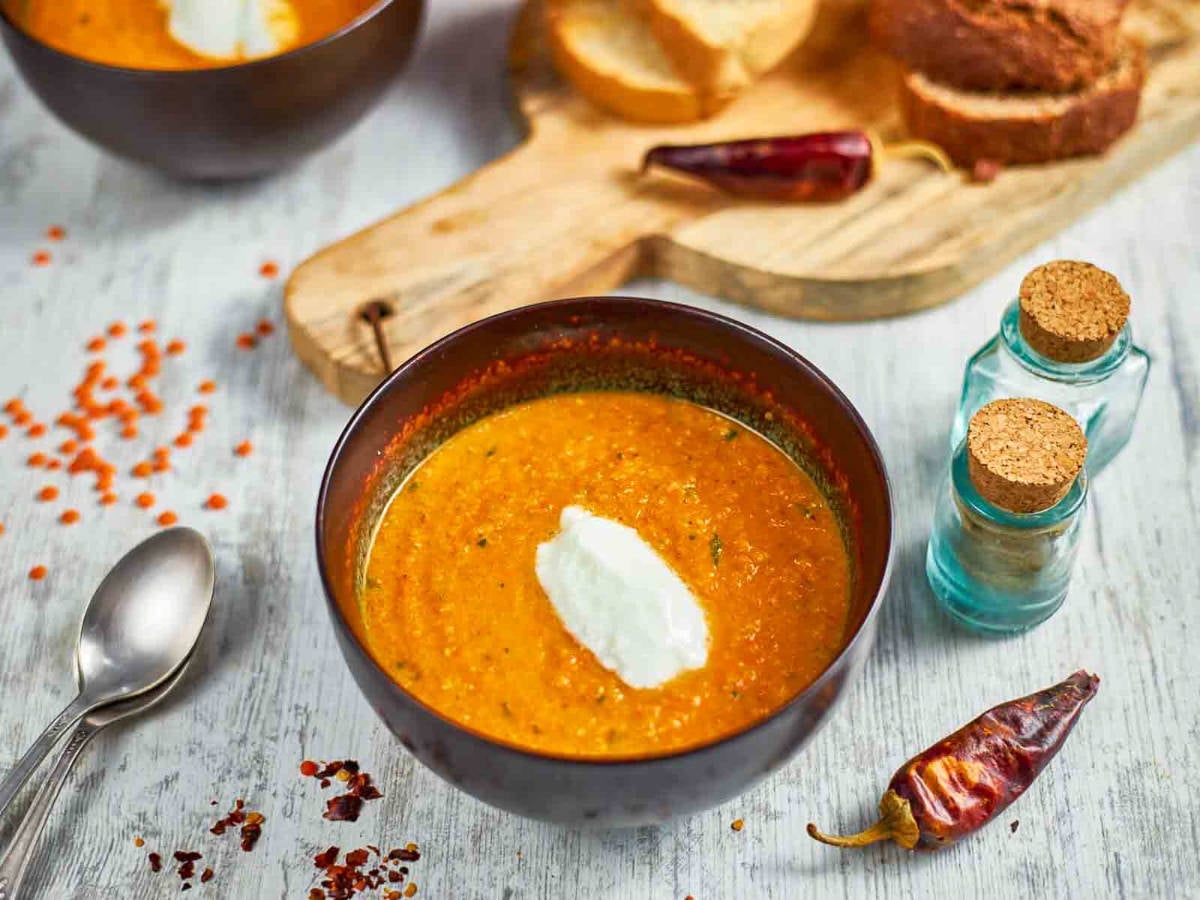 A bowl of spiced carrot soup placed on a white surface.